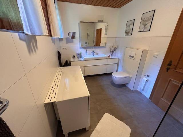 Modernes Badezimmer mit weißen Fliesen, Waschtisch und wandhängendem WC.