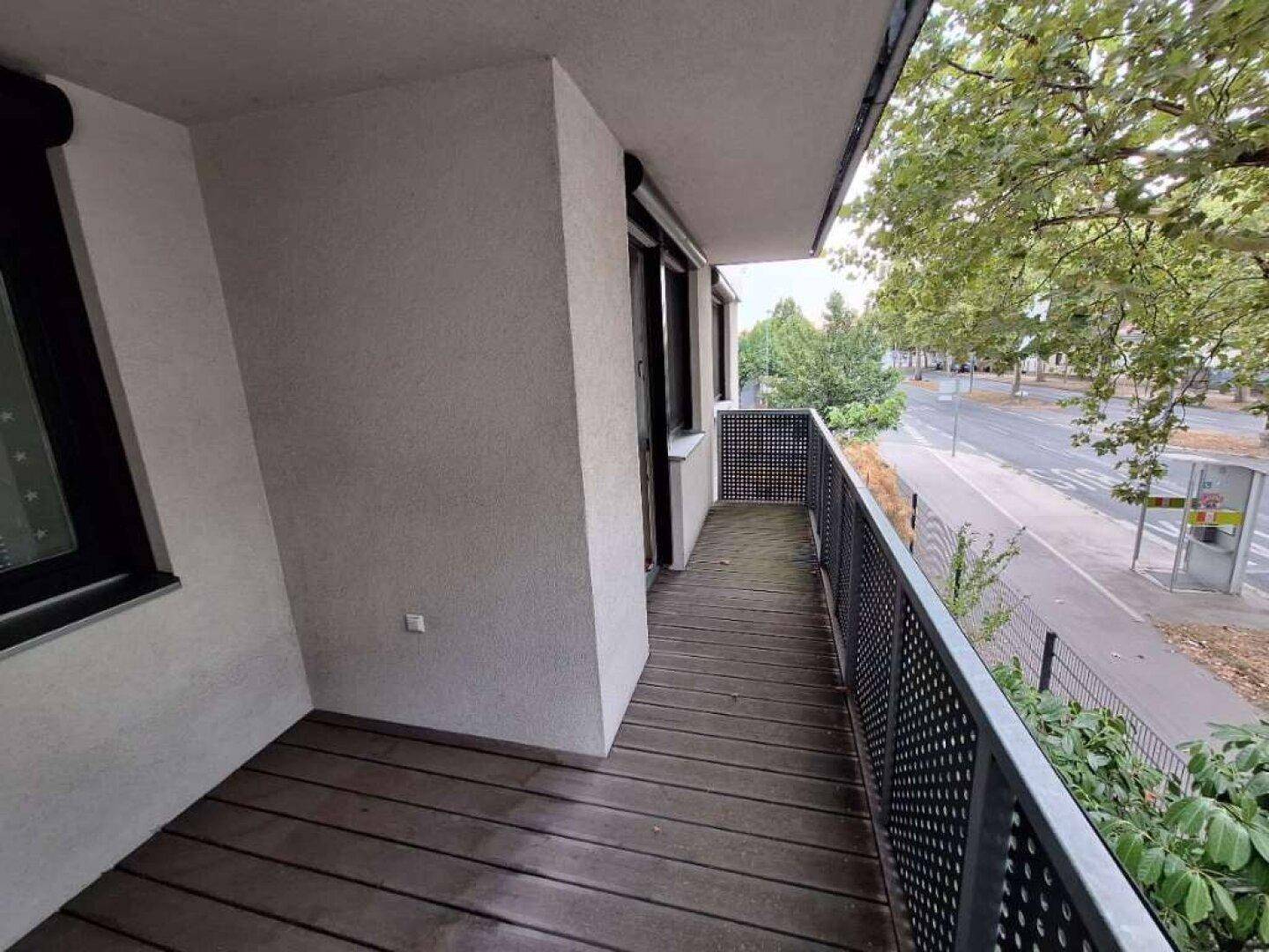 Langer Balkon mit Holzboden und Blick auf die Straße und umliegende Bäume.