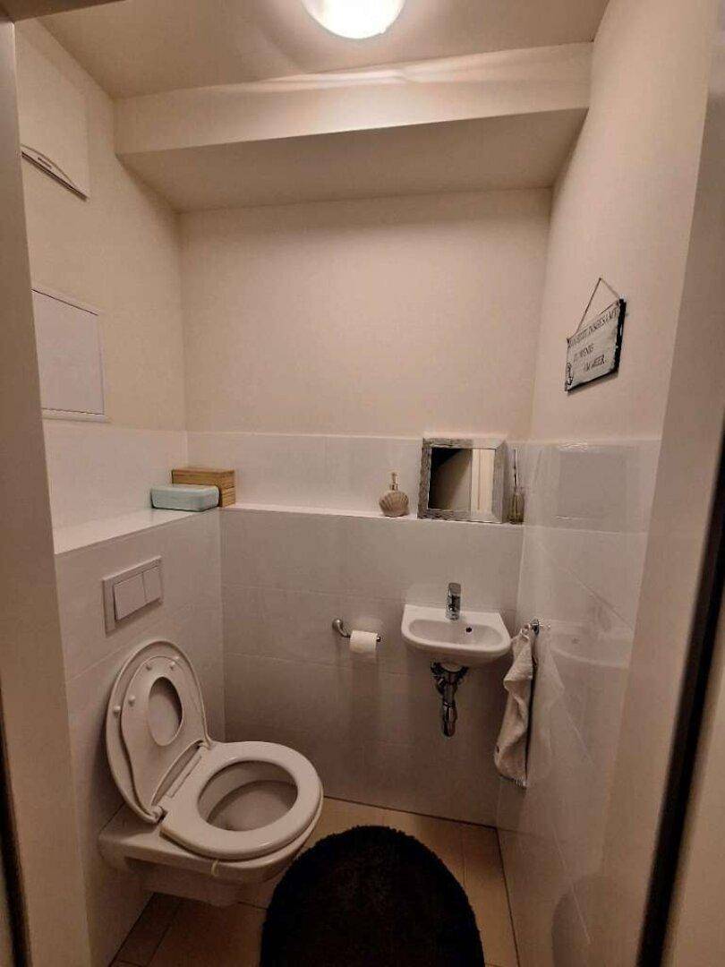 Kleines Gäste-WC mit weißen Fliesen, wandhängendem WC und kleinem Waschbecken.
