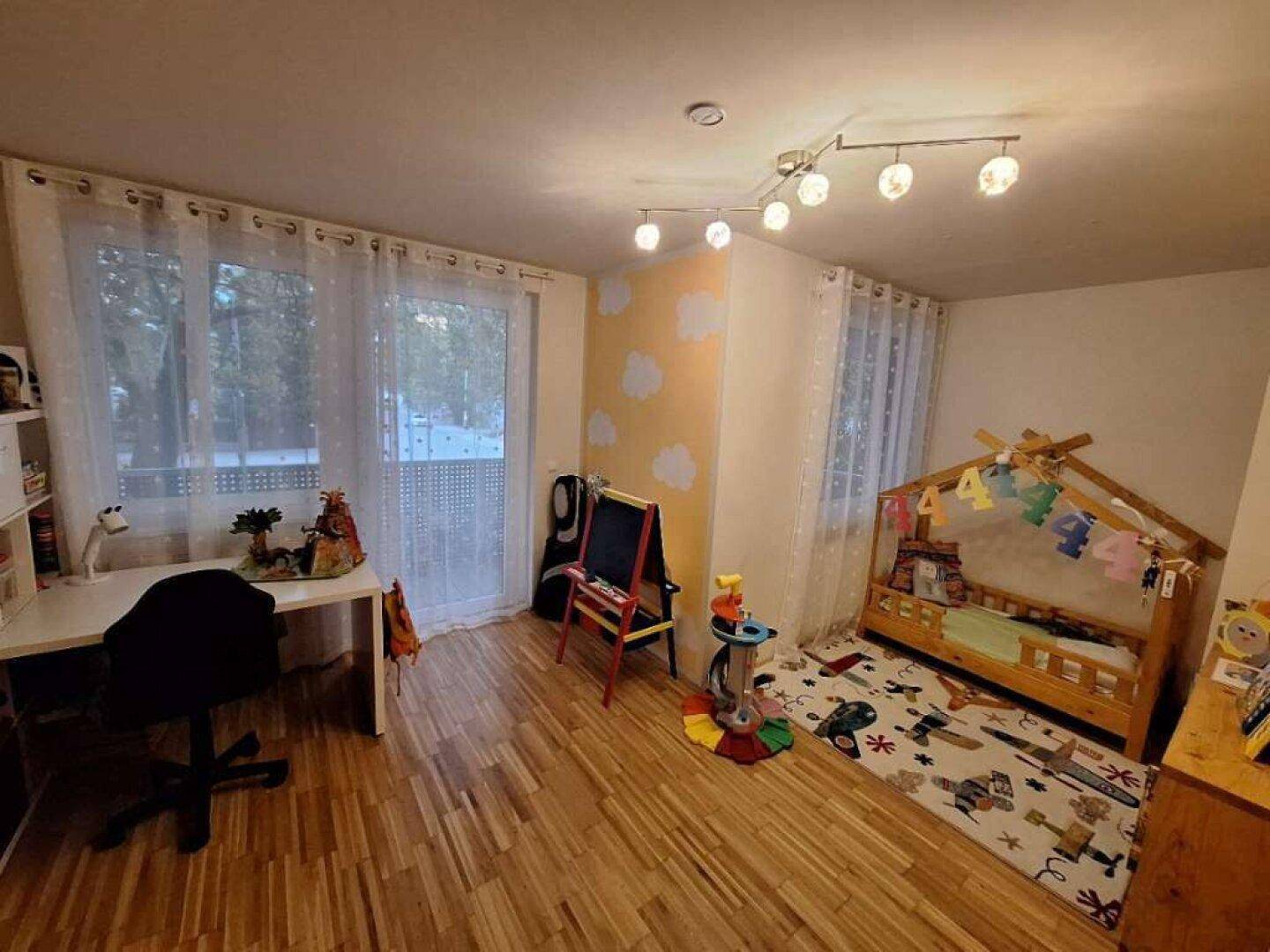 Kinderzimmer mit Holzboden, Schreibtisch und einem kleinen Bett, hell und freundlich gestaltet.