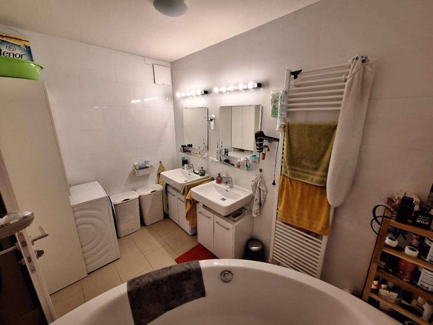 Modernes Badezimmer mit Doppelwaschbecken, Badewanne, Waschmaschine und beheiztem Handtuchhalter.