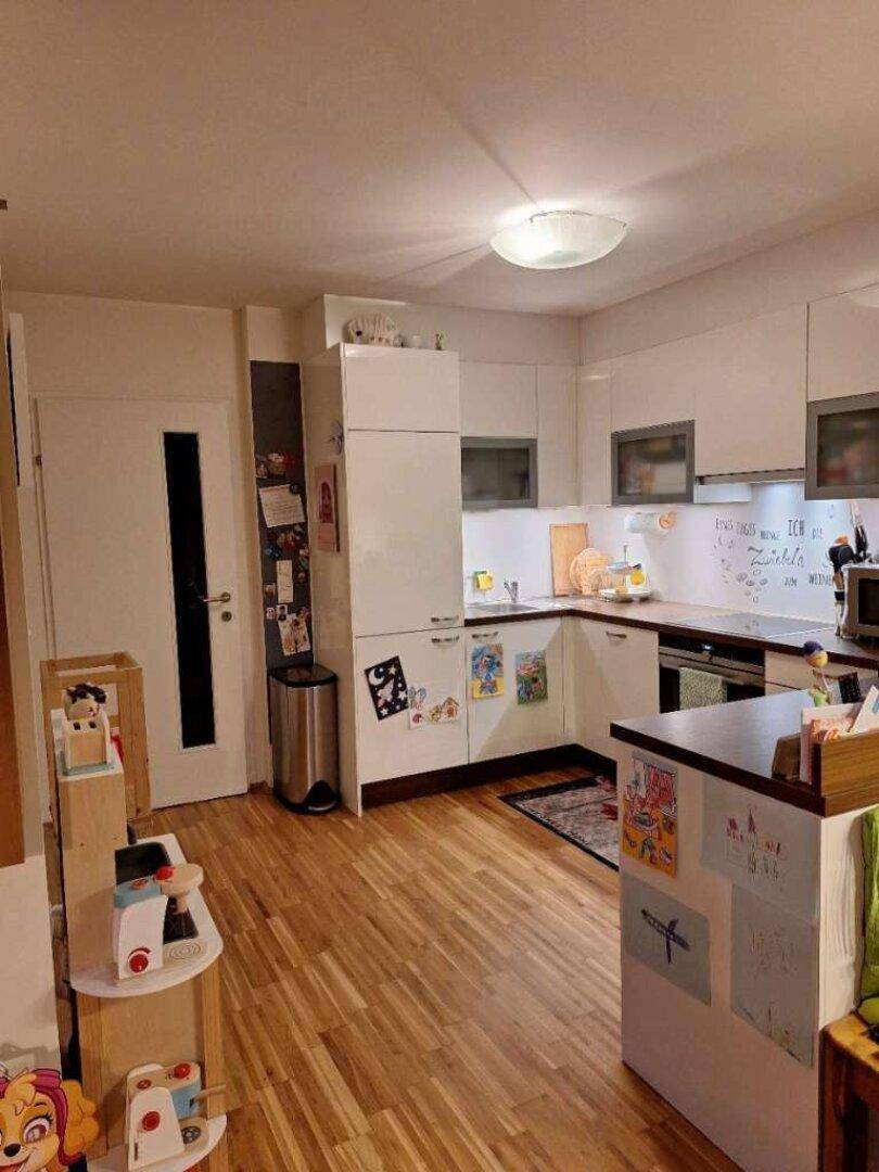 Moderne weiße Küche mit Holzboden und integrierten Geräten, offen zum Wohnbereich.