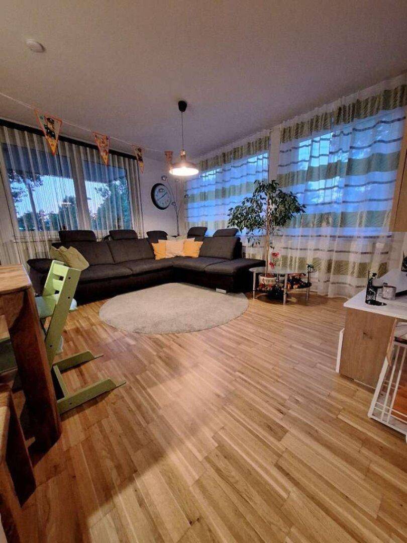 Geräumiges Wohnzimmer mit Holzboden, großer Eckcouch und viel Tageslicht.