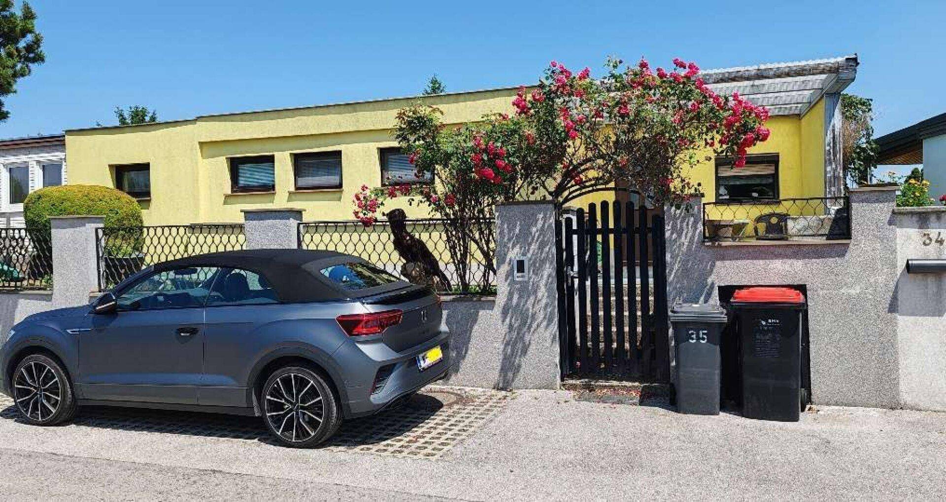 Gelbes Haus mit blühenden Rosensträuchern und einem gepflasterten Parkplatz vor dem Eingang.
