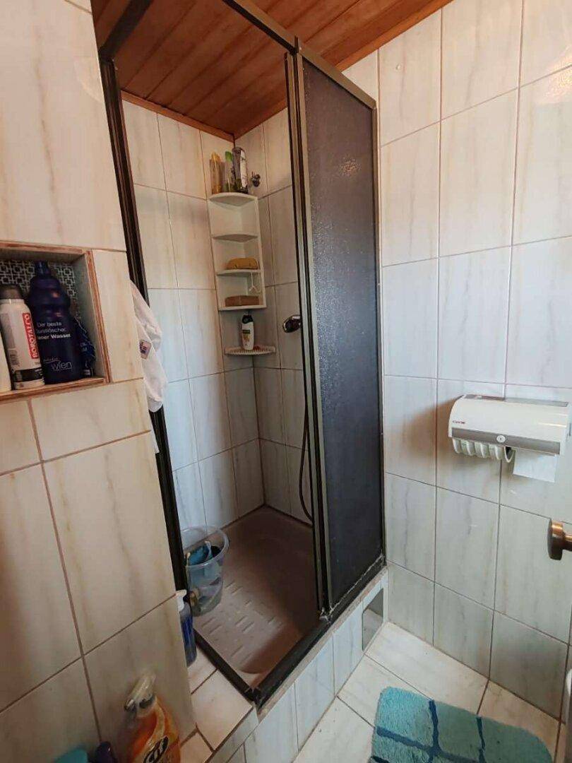 Badezimmer mit Duschkabine, gefliesten Wänden und einfacher Ausstattung.