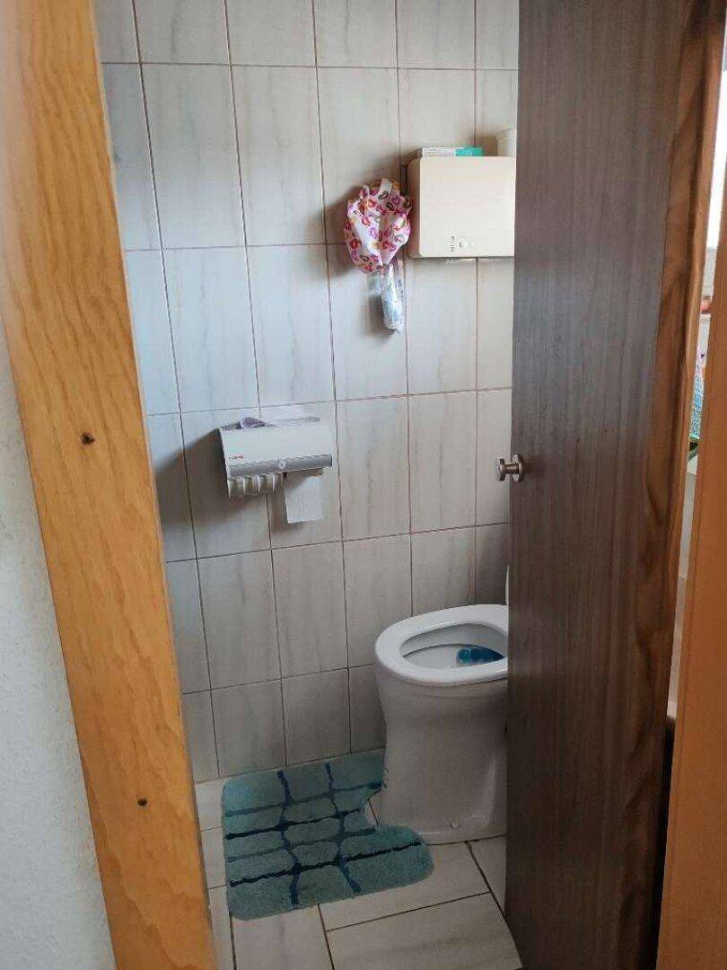 Separate Toilette mit gefliesten Wänden und einfacher, funktionaler Einrichtung.