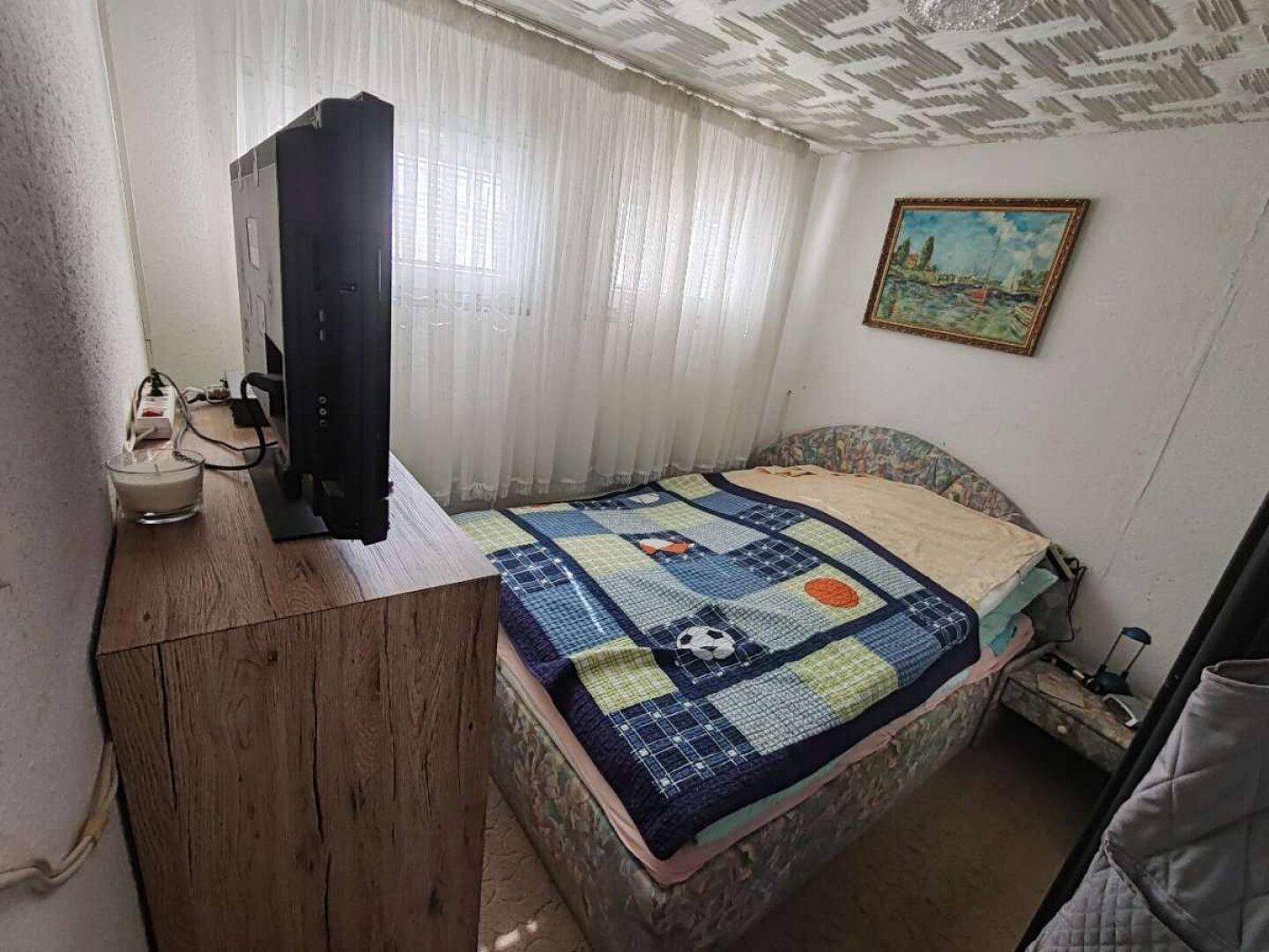 Kleines Schlafzimmer mit Einzelbett, Fernseher und Fenster für natürliches Licht.