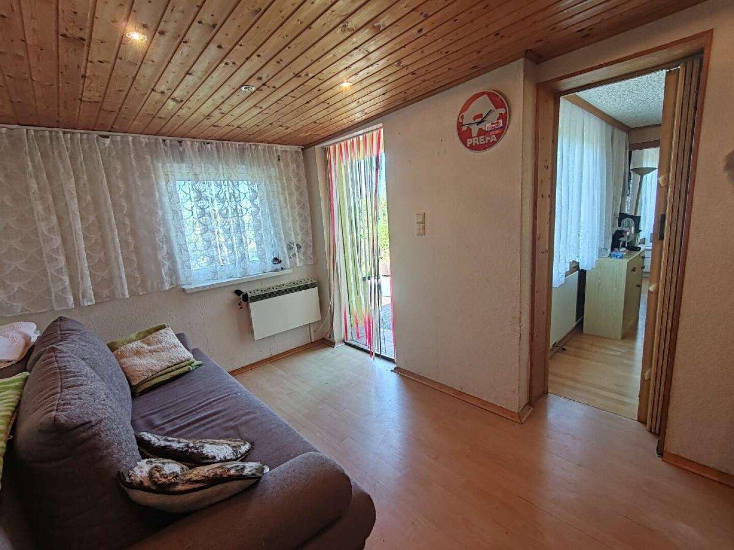 Gemütlicher Wohnbereich mit Holzdecke, Laminatboden und Zugang zu einem Außenbereich.