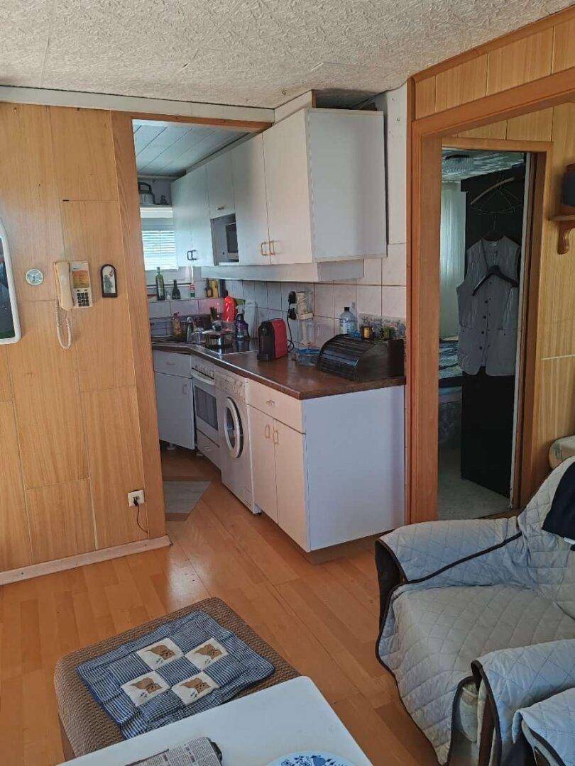 Kleine Küche mit weißen Schränken, Arbeitsplatte und Blick in den angrenzenden Wohnbereich.