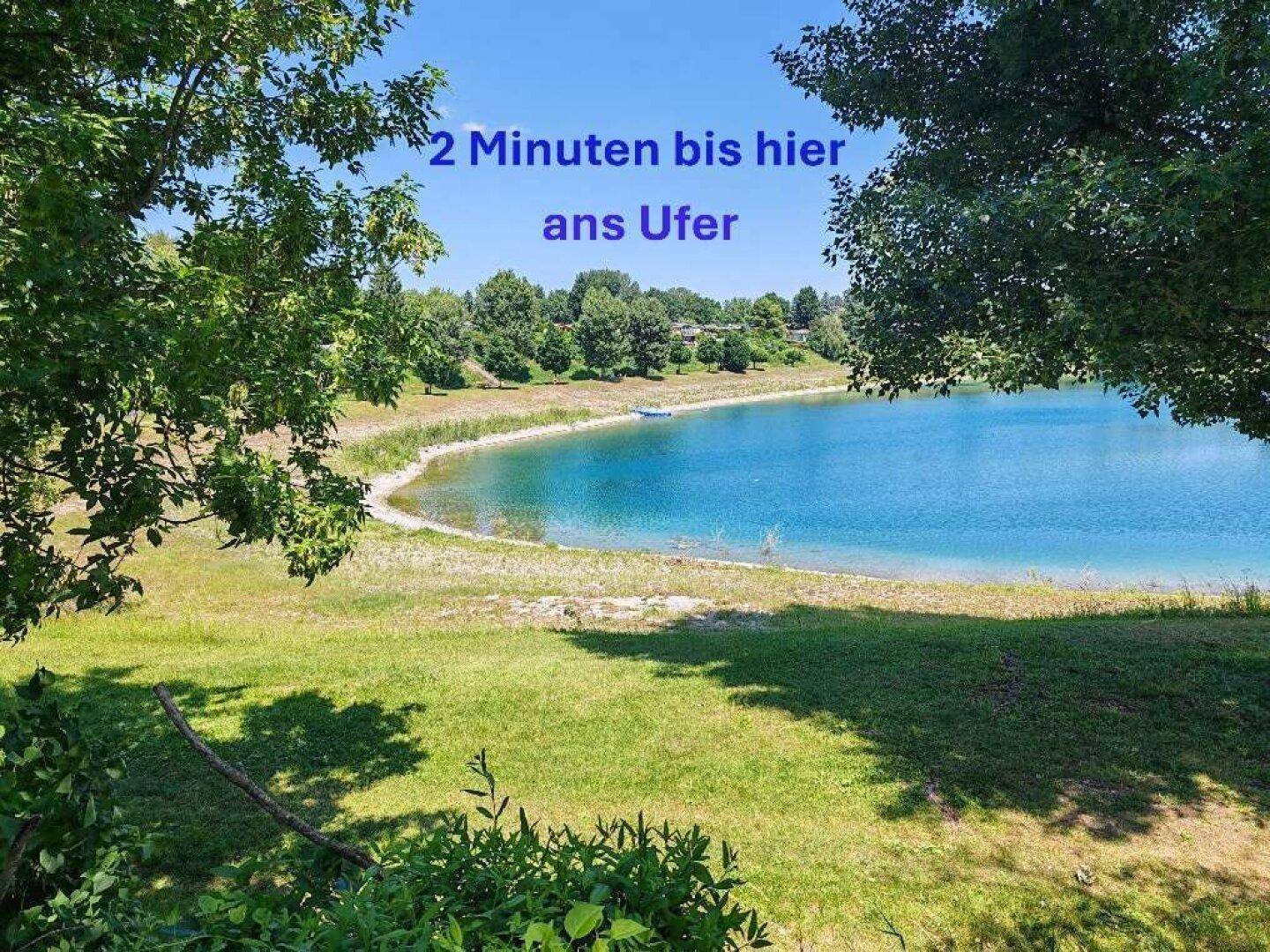 Malerischer Blick auf den See mit grünem Ufer und klarem Wasser unter blauem Himmel.