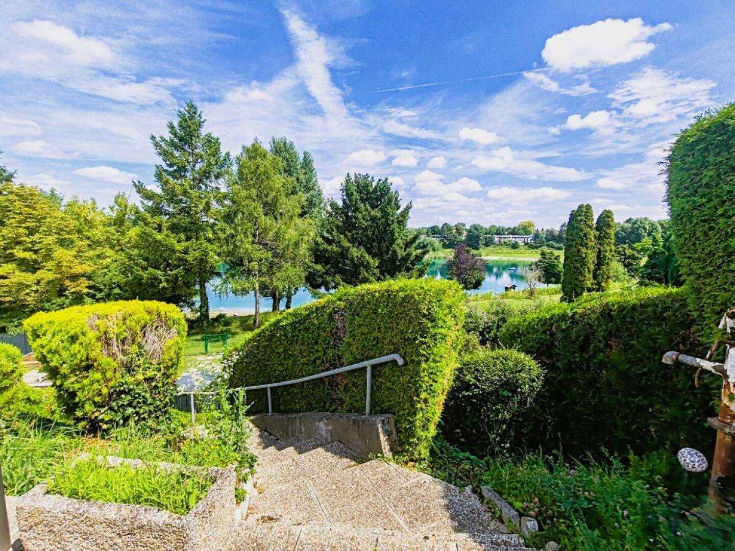 Treppenweg durch den grünen Garten mit weitem Blick auf den See und die Landschaft.