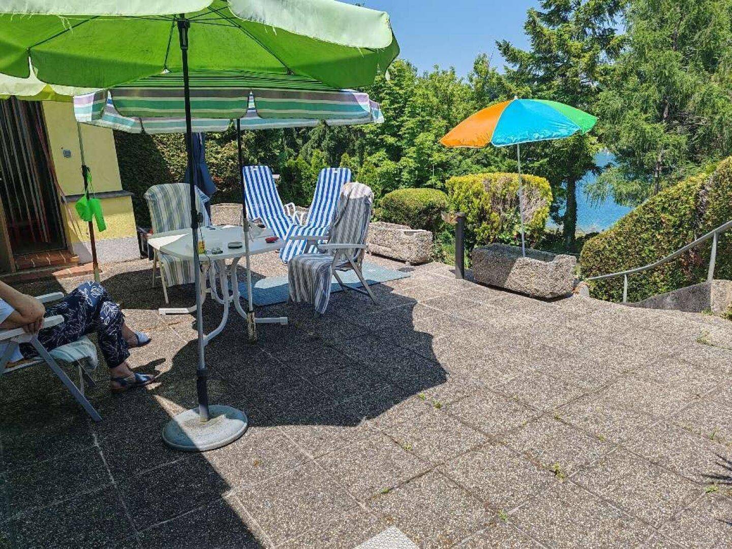 Sonniger Terrassenbereich mit Sitzgelegenheiten und Blick auf den See und die grüne Umgebung.