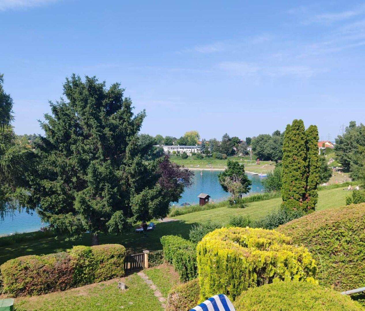 Weitläufiger Garten mit Blick auf den See und die umliegende Natur an einem sonnigen Tag.