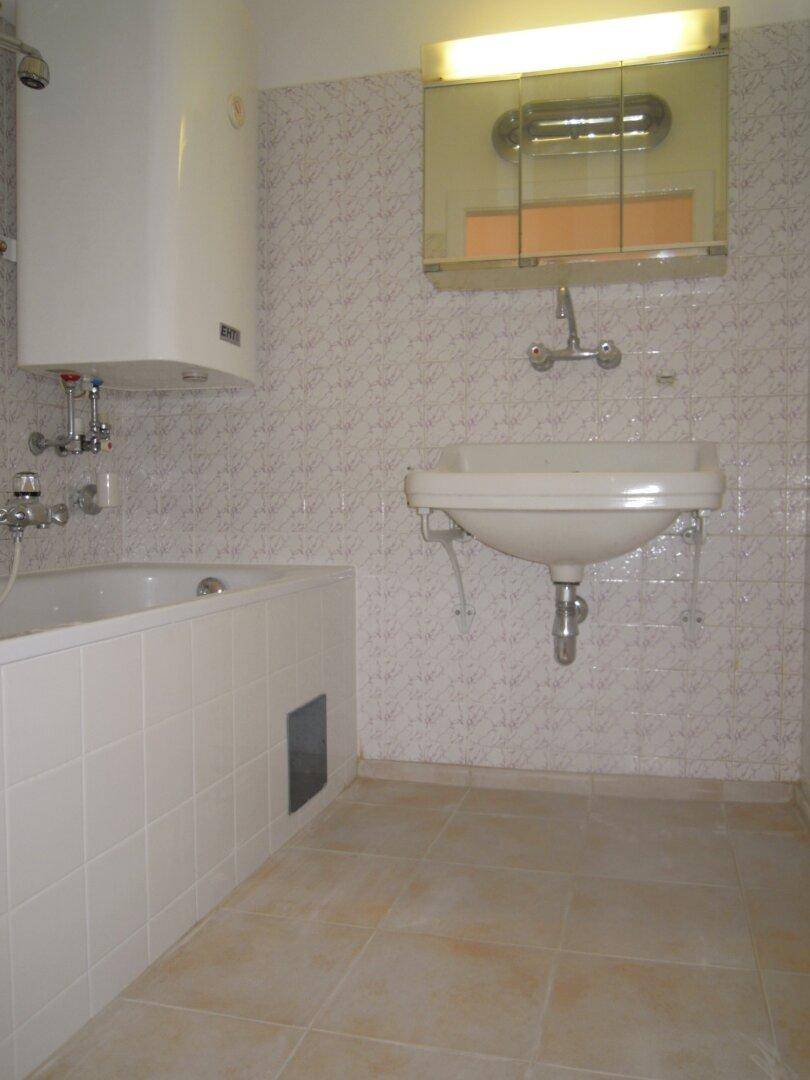 Badezimmer mit Badewanne, Waschbecken und hellen Fliesen, ausgestattet mit einem Spiegelschrank.