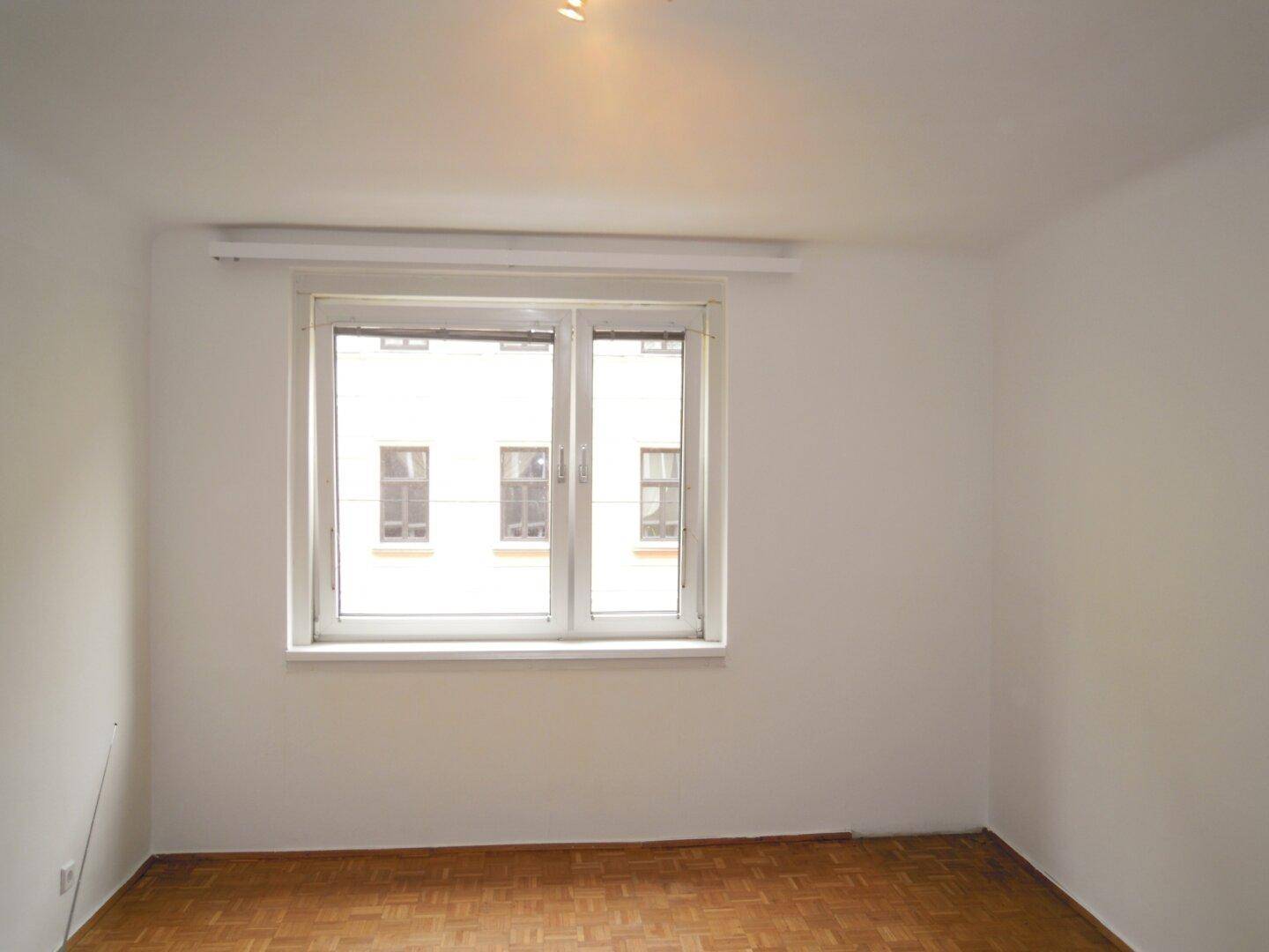 Freundliches Zimmer mit Parkettboden und Blick auf die gegenüberliegenden Gebäude.