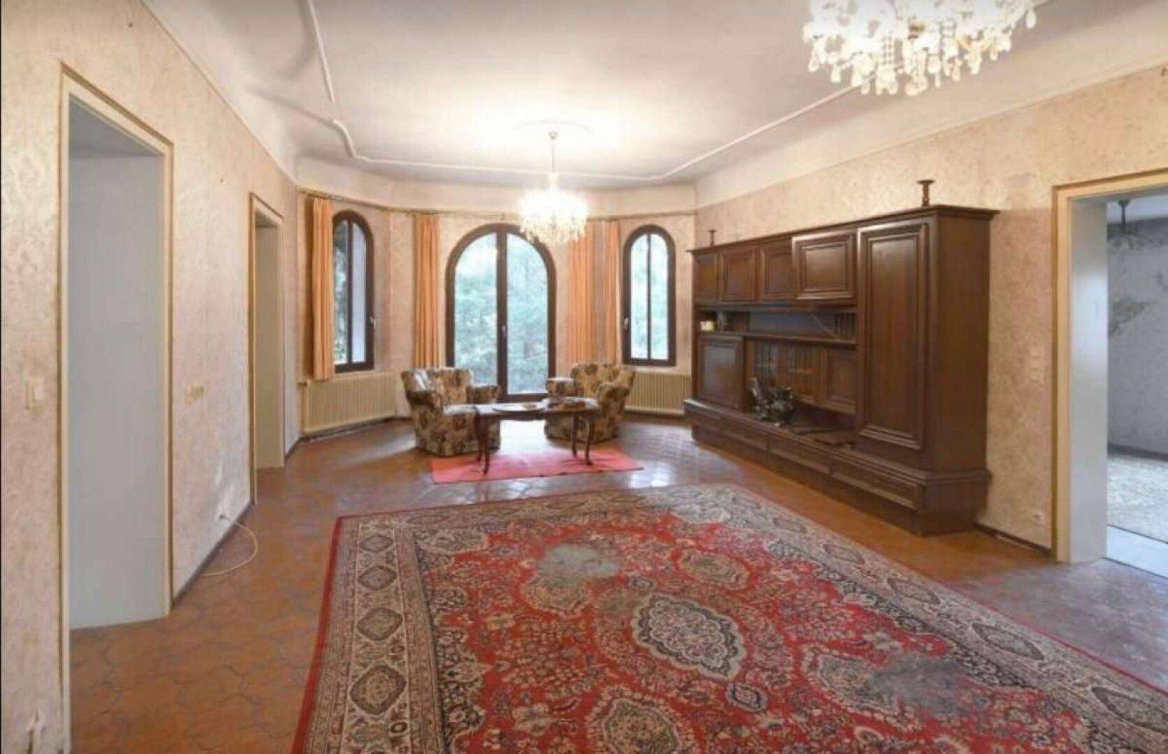 Geräumiges Wohnzimmer mit traditionellem Teppich, Rundbogenfenstern und klassischer Einrichtung.