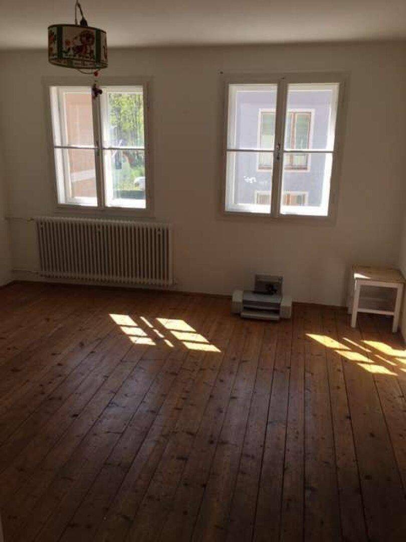 Helles Zimmer mit breiten Holzdielen, zwei Fenstern und viel Sonnenlicht.