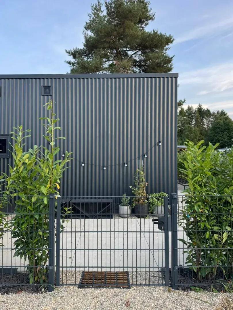 Dunkle Wellblechfassade eines modernen Gebäudes mit einem Gartentor und dekorativer Lichterkette.
