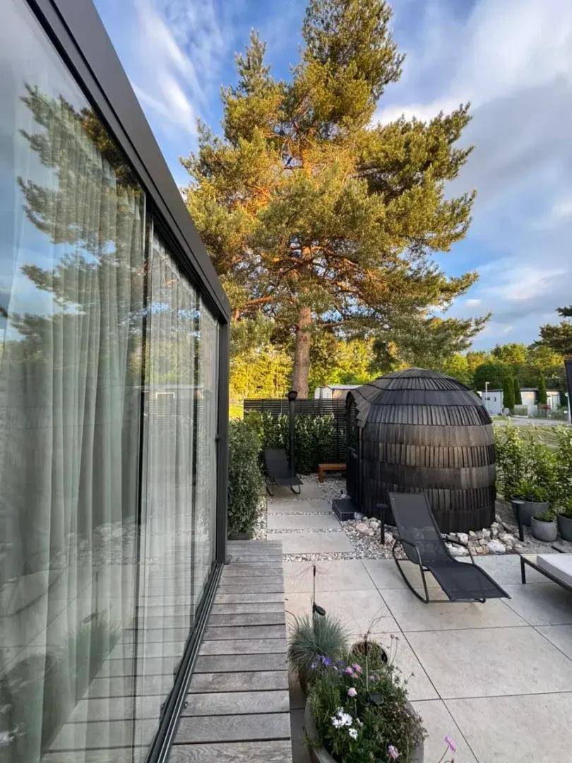 Große Glasfassade des Gebäudes öffnet sich zu einer Terrasse mit Liegestühlen und einem Saunafass.