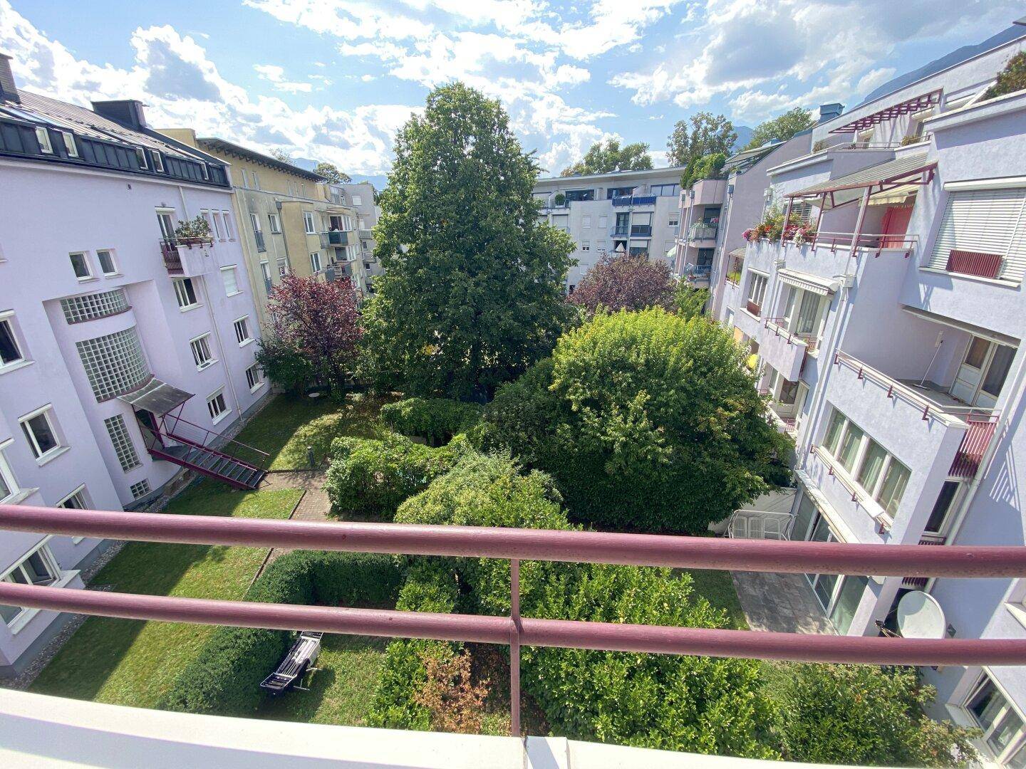 Balkon mit Blick auf einen gepflegten grünen Innenhof, umgeben von Gebäuden.