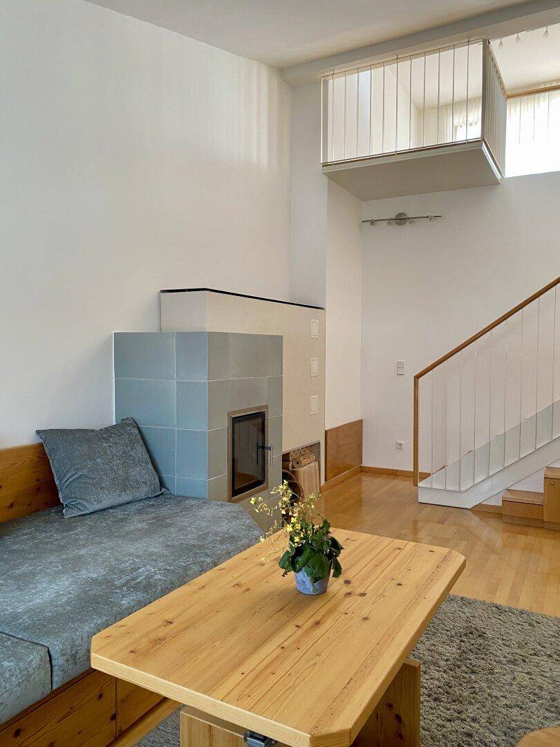 Geräumiges Wohnzimmer mit Kachelofen, Holzboden und offener Galerie im Obergeschoss.