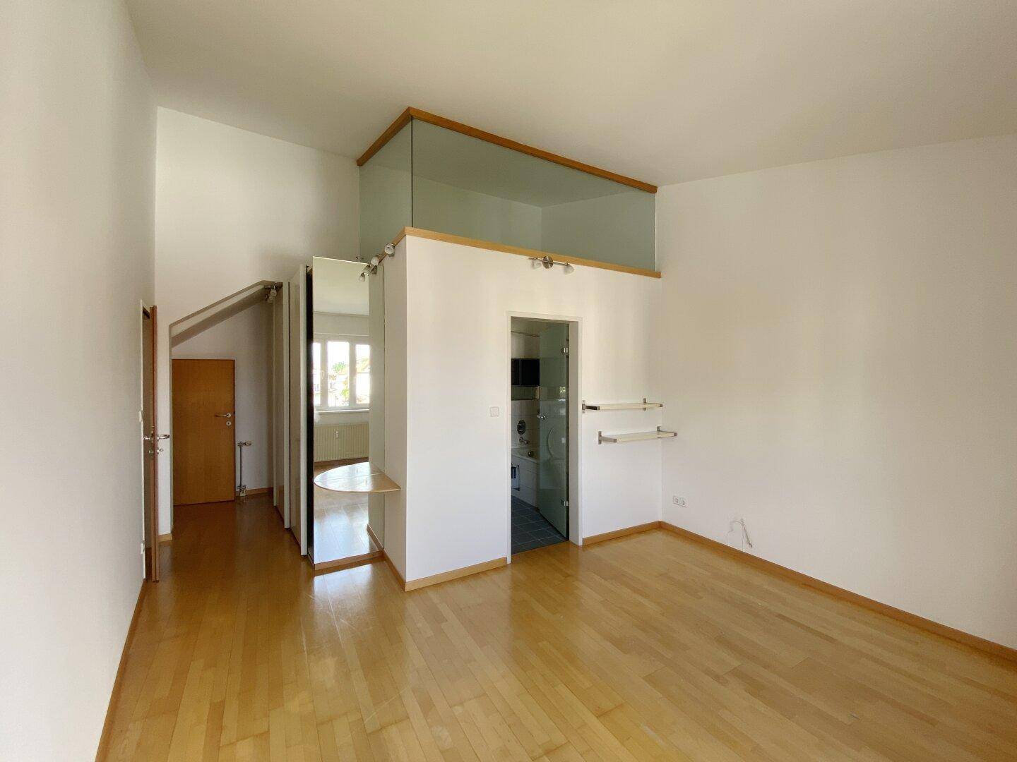 Offener Raum mit Holzparkett, hoher Decke und einer Galerie mit Glasgeländer.