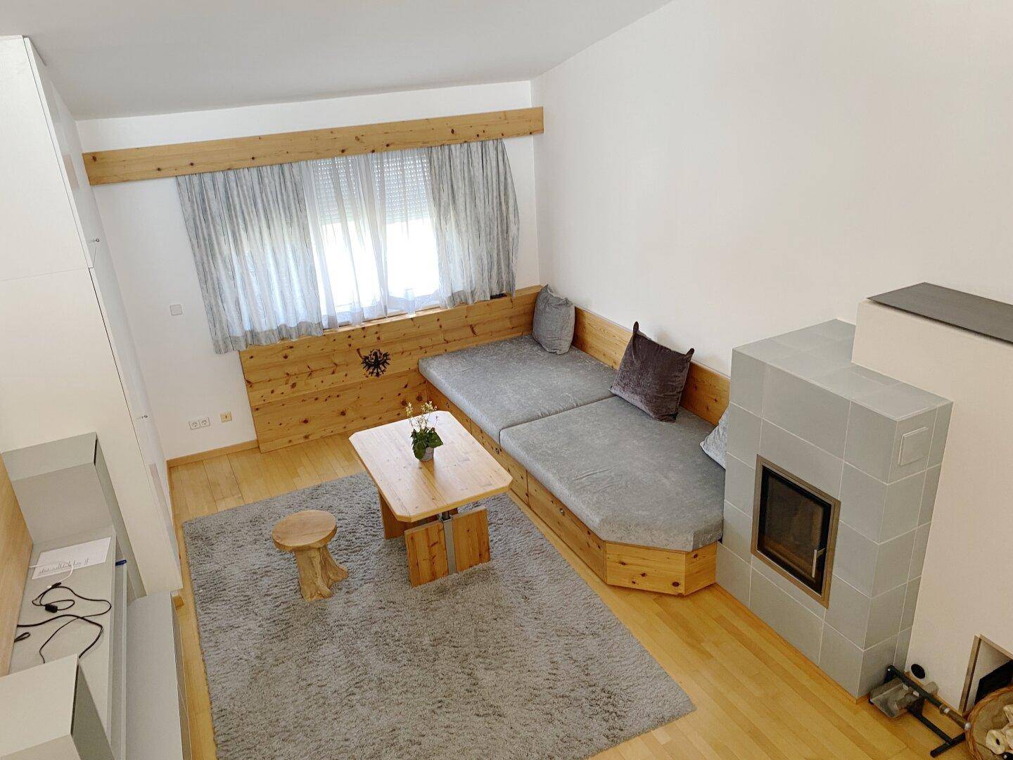 Wohnzimmer mit traditionellem Kachelofen, Holzbänken und einem weichen Teppich.