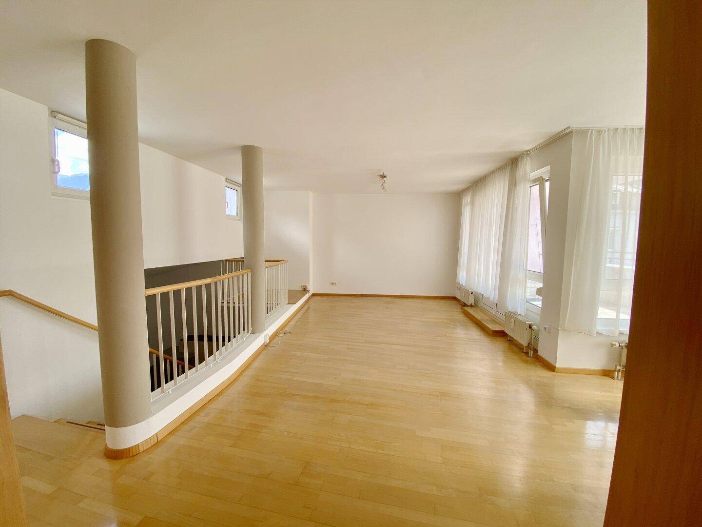 Großer, offener Wohnbereich mit Holzparkett, hohen Decken und viel Tageslicht.
