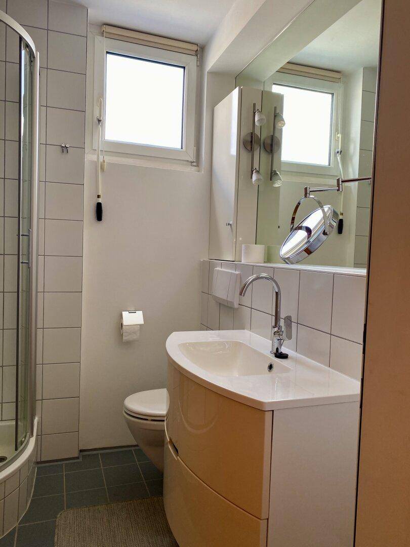 Helles Badezimmer mit Dusche, WC, Waschtisch und Fenster für Tageslicht.