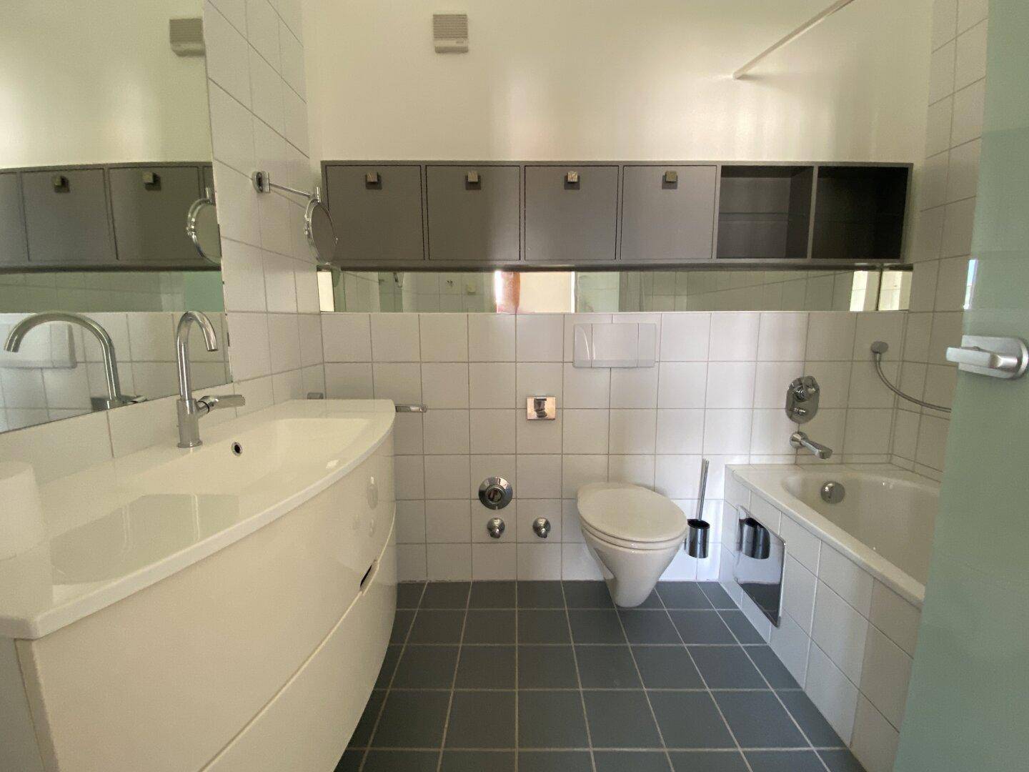 Modernes Badezimmer mit Badewanne, WC, Waschtisch und grauen Bodenfliesen.
