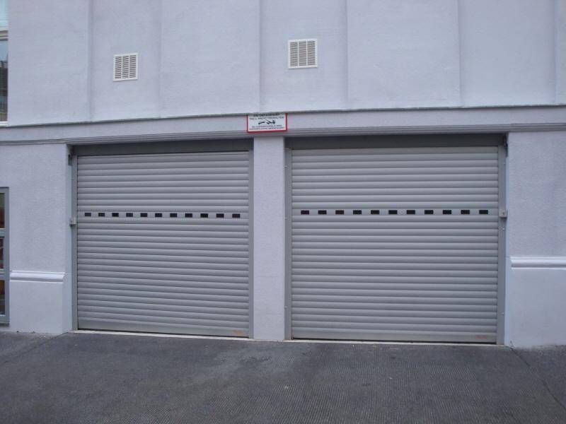 Zwei graue Rolltore einer Tiefgarage oder Parkgarage an einer schlichten Gebäudefassade.