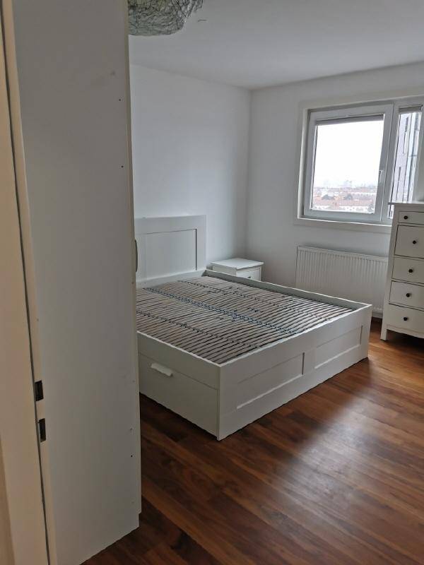 Helles Schlafzimmer mit Holzboden, weißem Bett und Fenster mit Blick nach draußen.