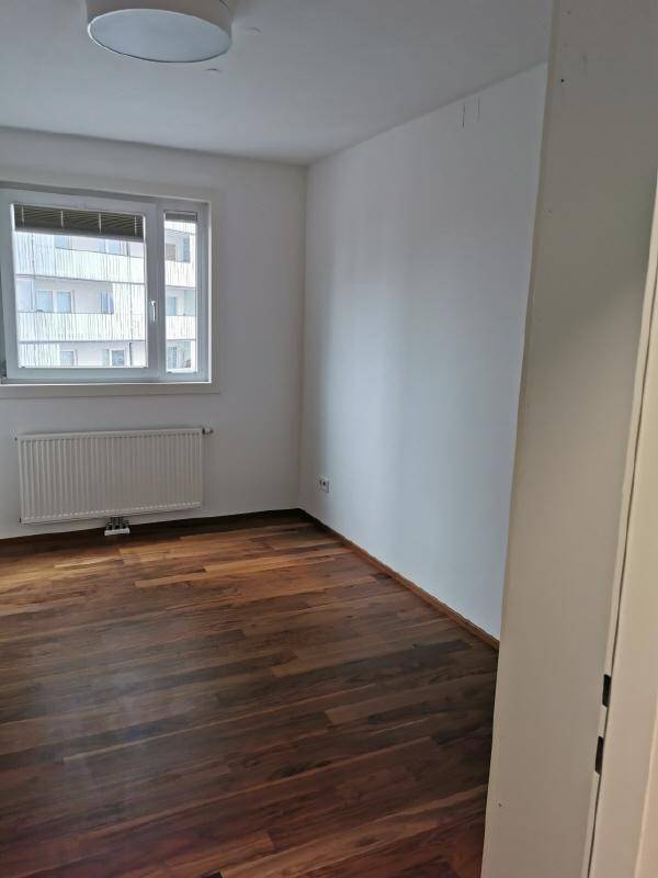 Leeres Schlafzimmer mit Holzboden, Heizkörper und großem Fenster für viel Tageslicht.