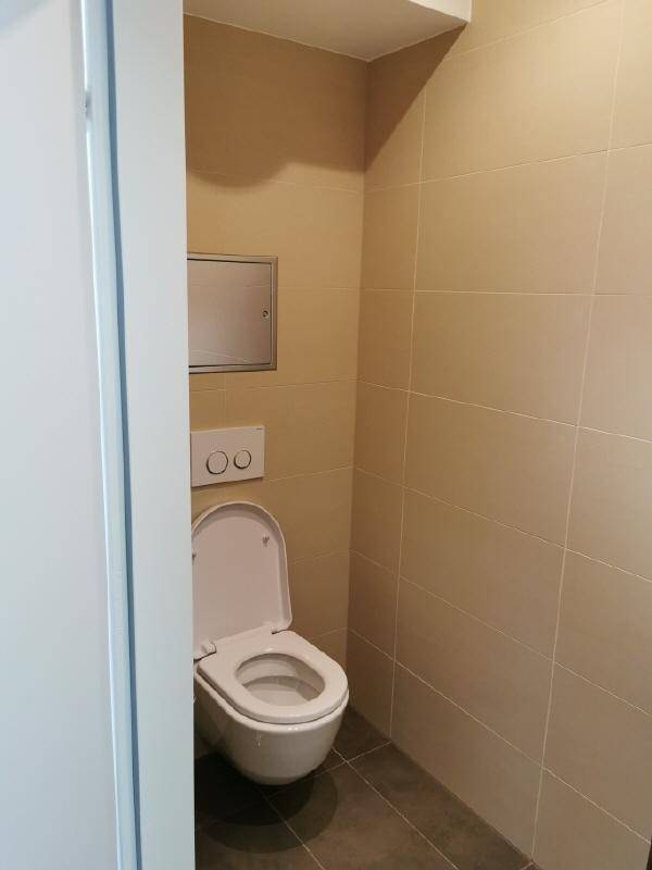 Separates WC mit wandhängender Toilette und beigefarbenen Wandfliesen.