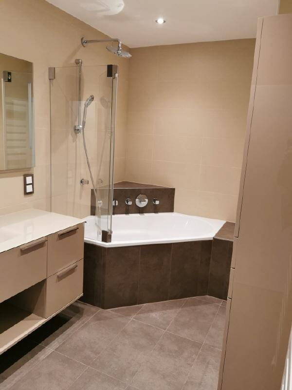 Elegantes Badezimmer mit Eckbadewanne, moderner Dusche und beigefarbenen Fliesen.