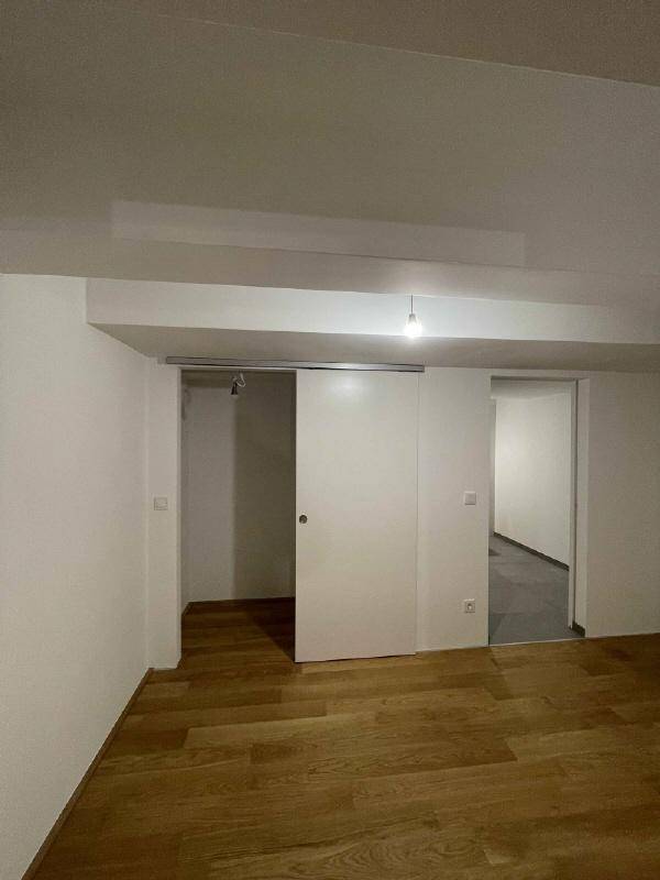 Heller Raum mit Holzboden und einer modernen Schiebetür zu einem weiteren Bereich.