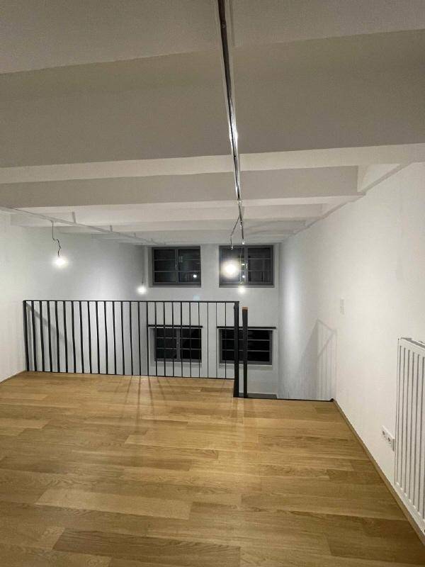Mezzanine-Ebene mit Holzboden, schwarzem Geländer und Blick auf die Fenster.