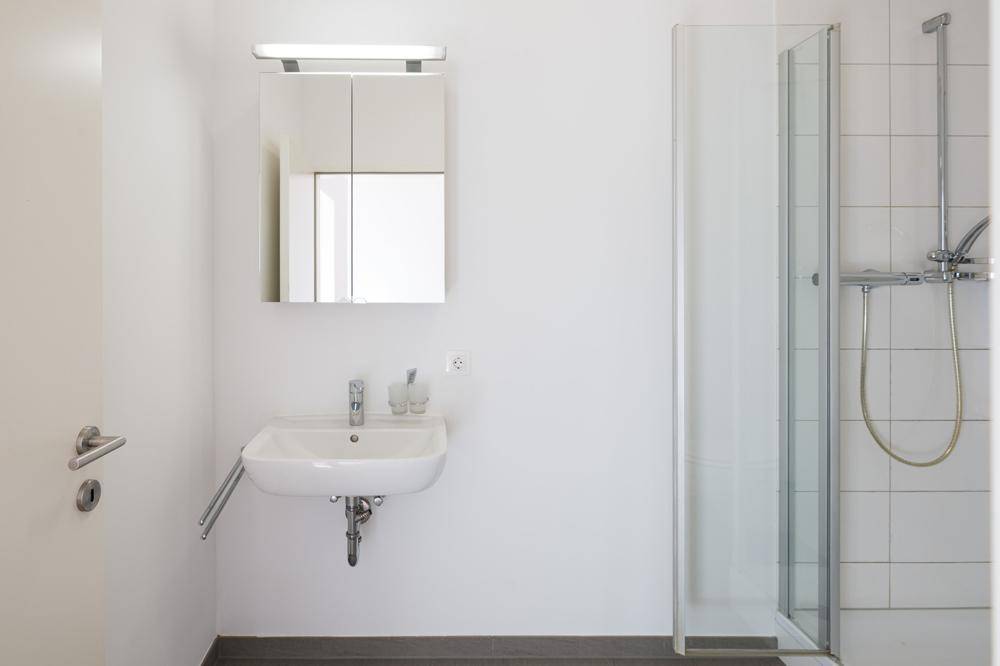 Modernes Badezimmer mit Duschkabine, Waschbecken und Spiegelschrank, in hellem Design gehalten.