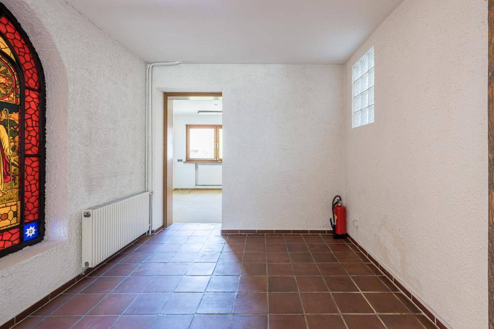 Flur mit Terrakotta-Fliesenboden, weiß getünchten Wänden und einem farbigen Buntglasfenster.
