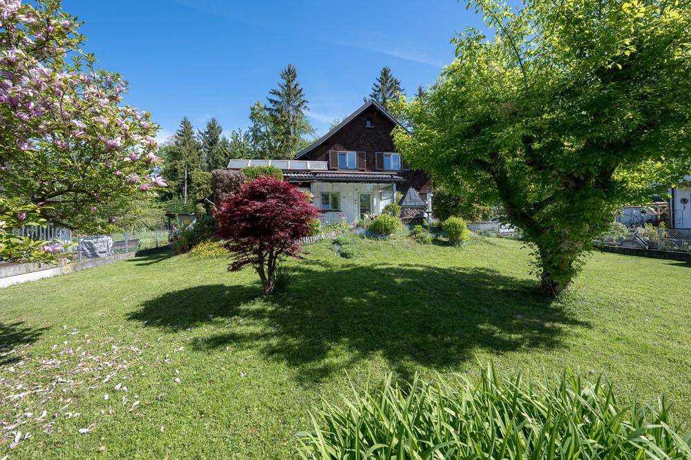 Gepflegtes Einfamilienhaus mit weitläufigem Rasen, blühenden Bäumen und umgebender Natur.