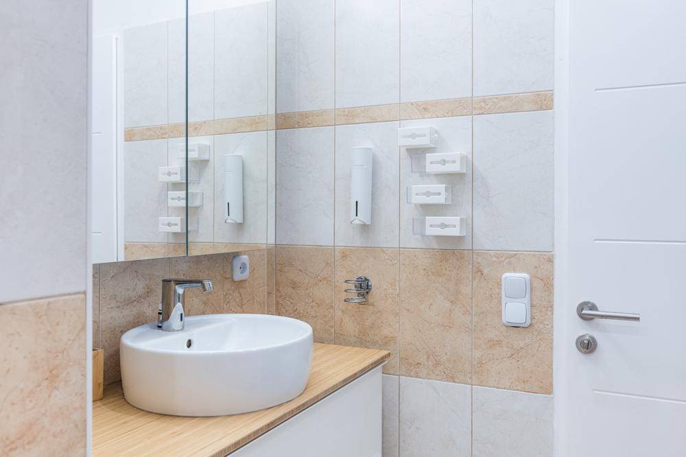 Modernes Badezimmer mit rundem Waschbecken, Holzplatte und hellen Fliesen an den Wänden.