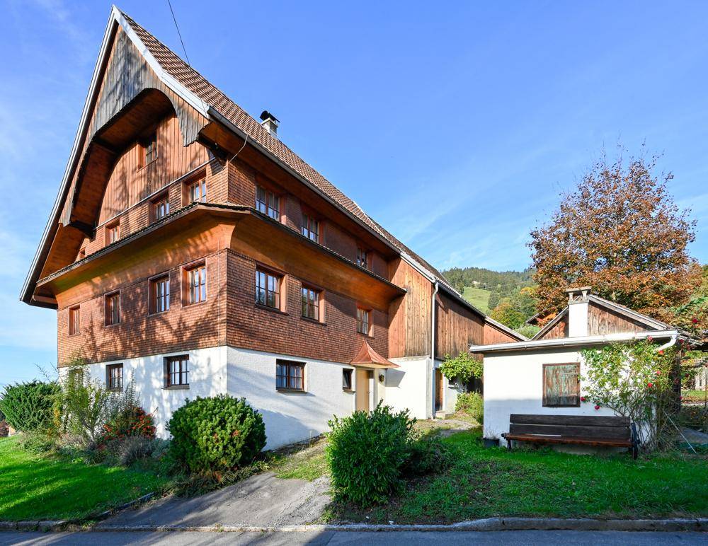 Traditionelles Holzhaus mit Satteldach, Nebengebäude und gepflegtem Vorgarten.