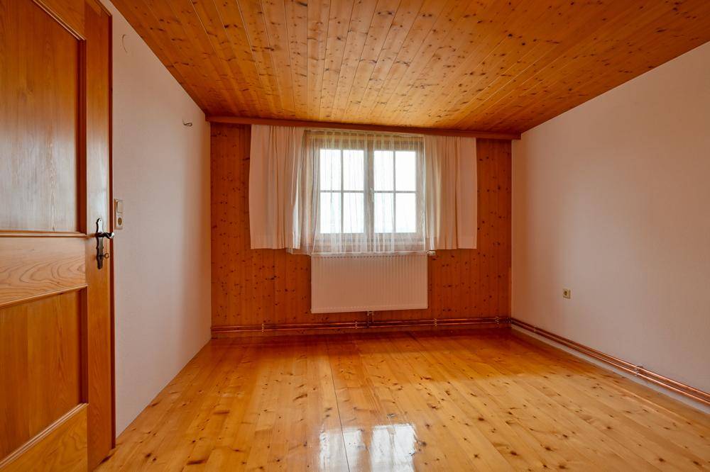 Gemütliches Zimmer mit Holzboden, Holzdecke und einer Holztür, gut beleuchtet durch ein Fenster.