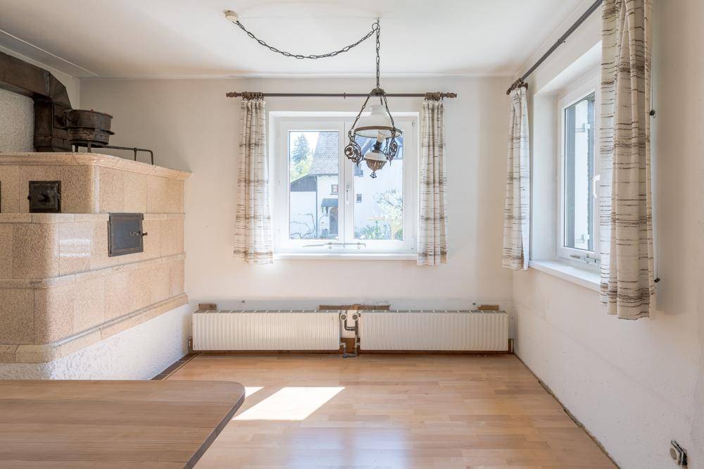 Gemütlicher Raum mit traditionellem Kachelofen, Holzfußboden und Fenstern mit Vorhängen.