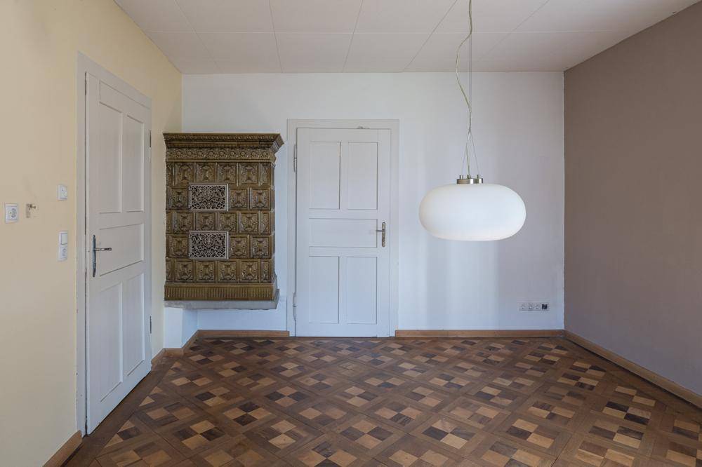 Geräumiger Raum mit traditionellem Parkettboden und einem Kachelofen an der Wand.