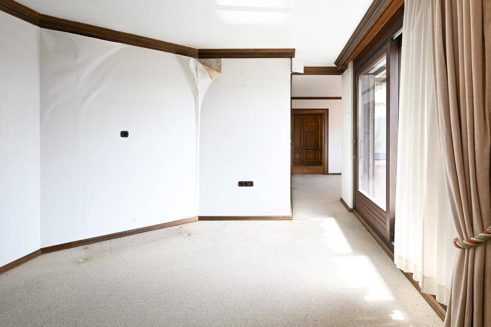 Leerer Raum mit Teppichboden und Spuren von abgelöster Tapete, bereit für Renovierung.