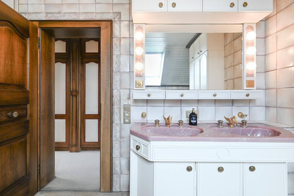 Badezimmer mit doppelten rosa Waschbecken, weißen Fliesen und einem großen Spiegelschrank.