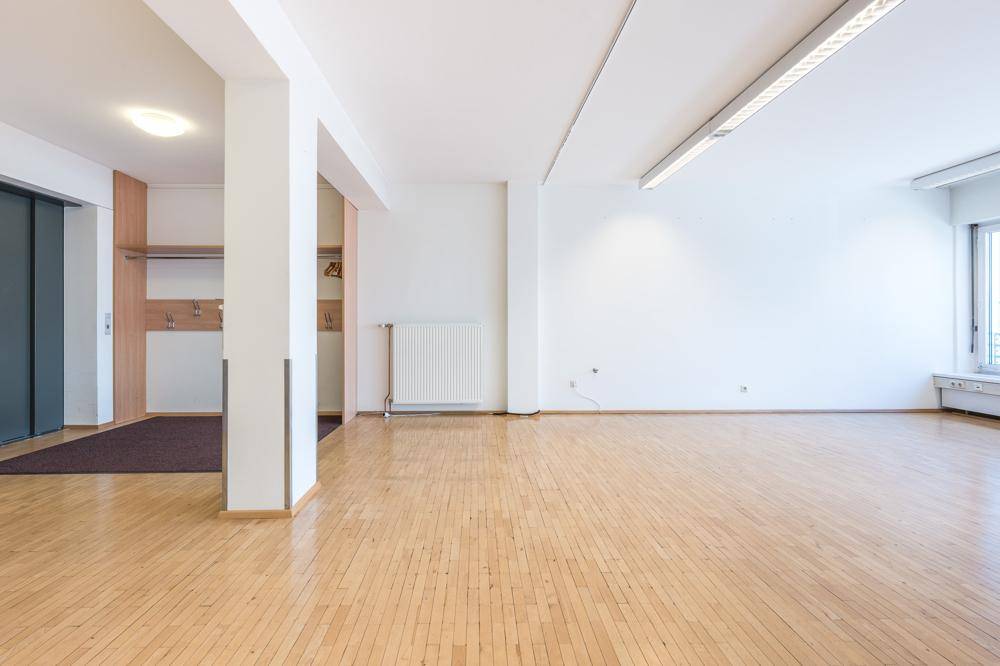 Geräumiger, heller Büroraum mit Holzboden, weißen Wänden und Blick auf den Eingangsbereich.