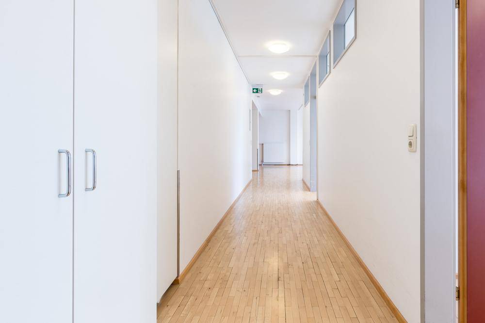 Langer, heller Flur mit Holzboden, weißen Einbauschränken und Deckenbeleuchtung, der zu weiteren Räumen führt.