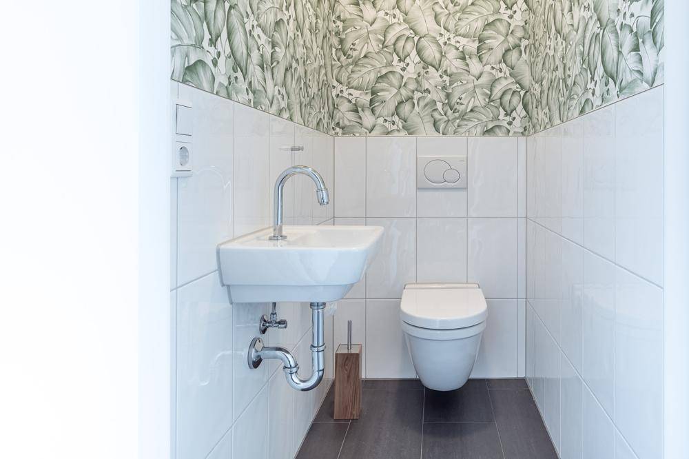 Kleines Gäste-WC mit modernem Waschbecken, Wand-WC und auffälliger Tapete.